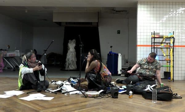 Performers seated on the floor among scattered materials.