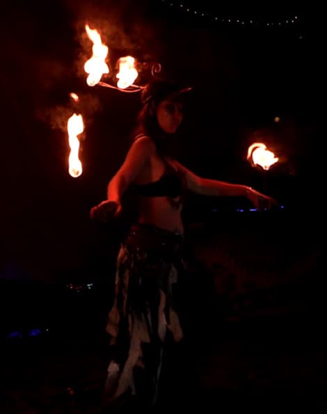 A fire performer with handheld flames in the dark.